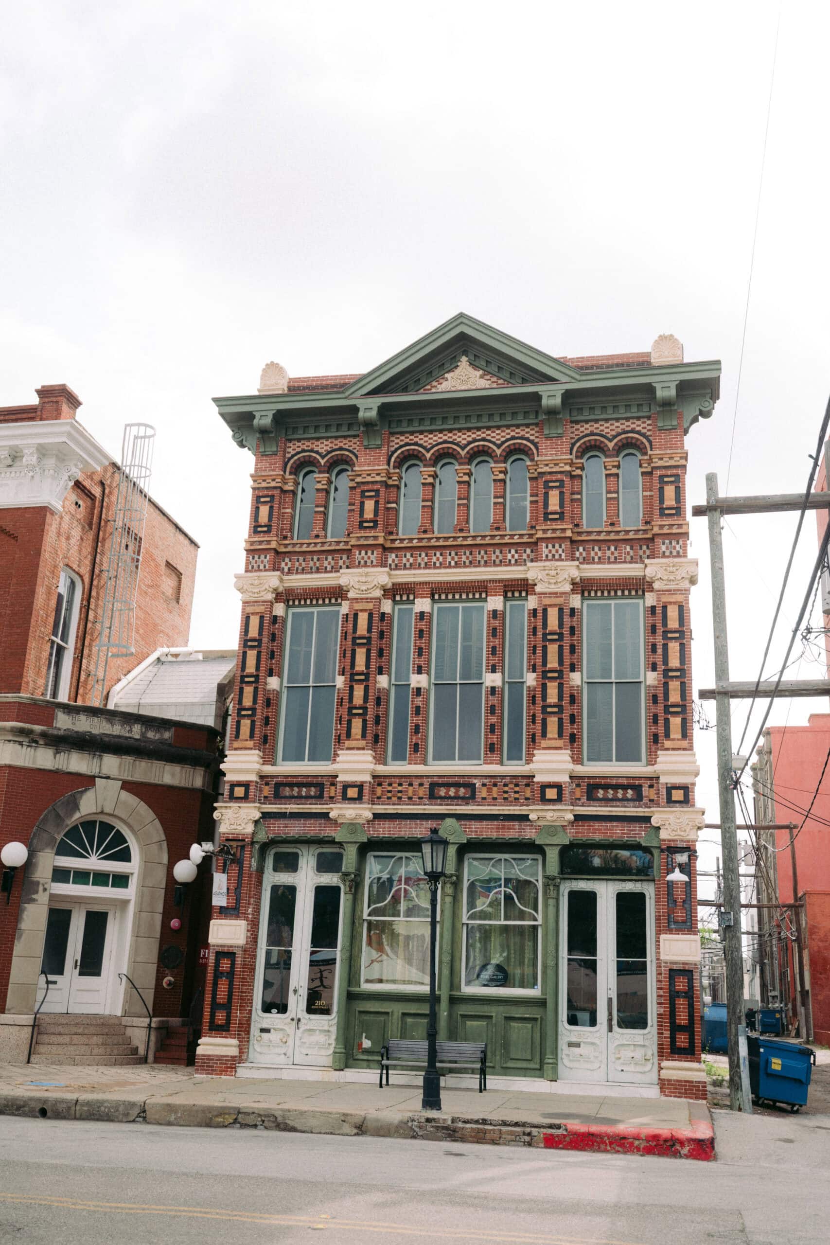 The Trueheart-Adriance Building in Texas is a three-story brick historic building with intricate decorative patterns on the facade, large windows, and green detailing on the ground floor. A black lamp post stands in front, with adjacent buildings partially visible. - McNatt Contracting