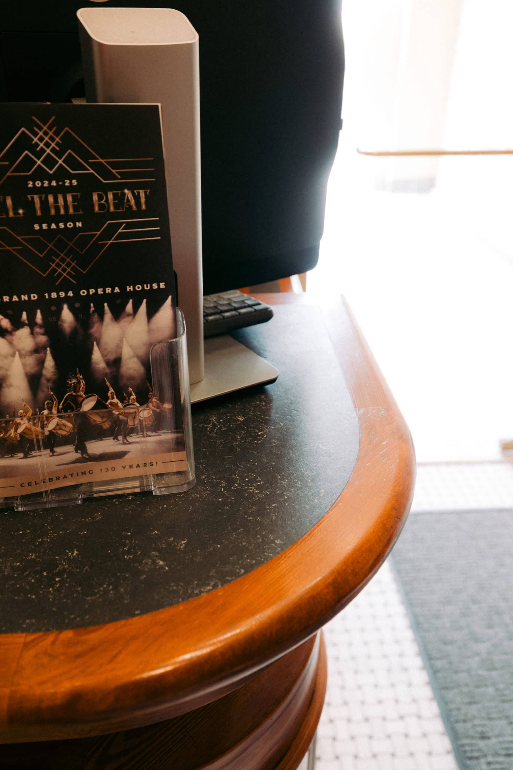 A brochure advertising the 2024-25 season at the Grand 1894 Opera House is displayed on a wooden counter next to a computer monitor and keyboard. - McNatt Contracting